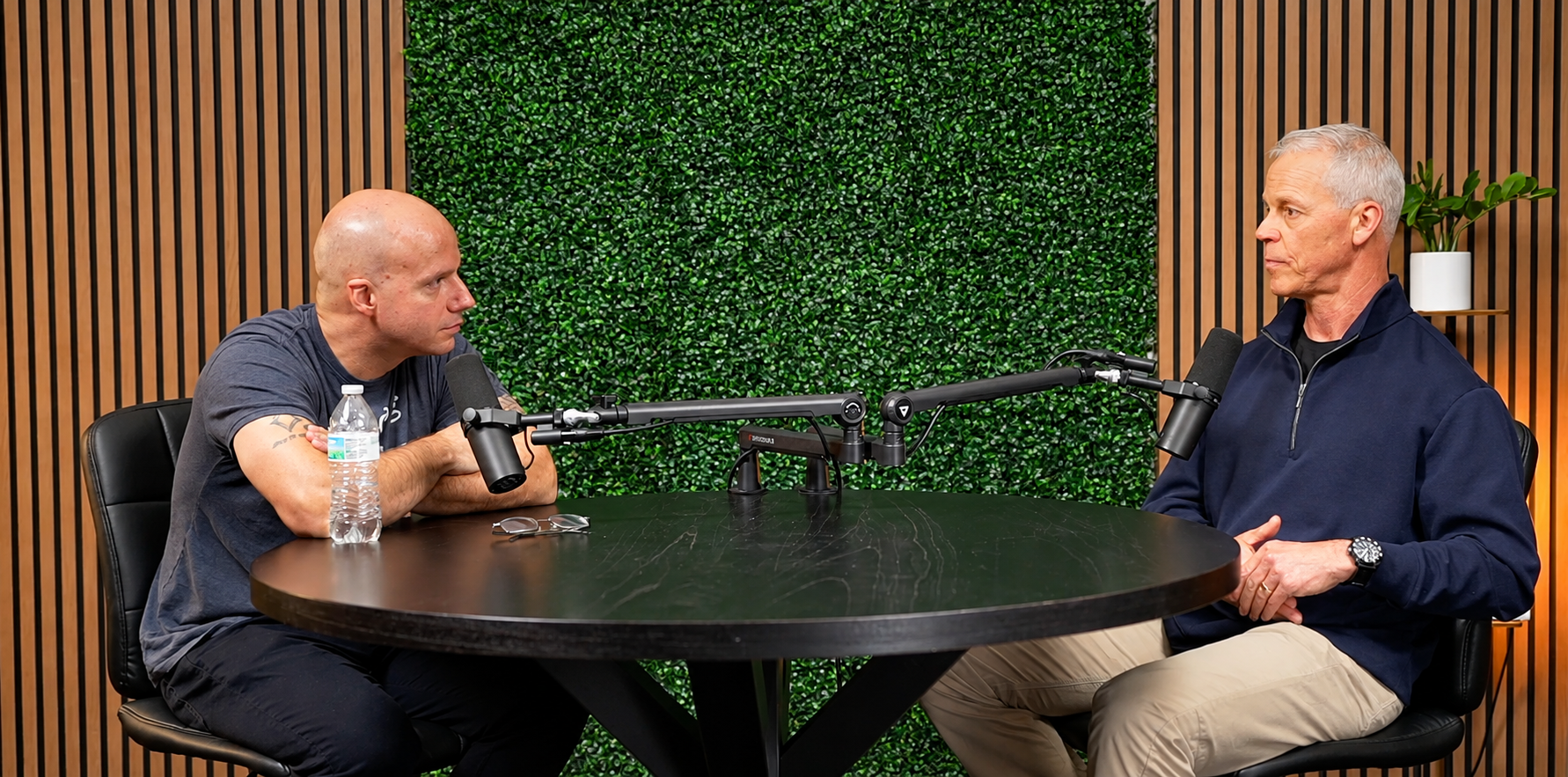 Calvin Smith interviewing a guest across a studio table with podcast microphones