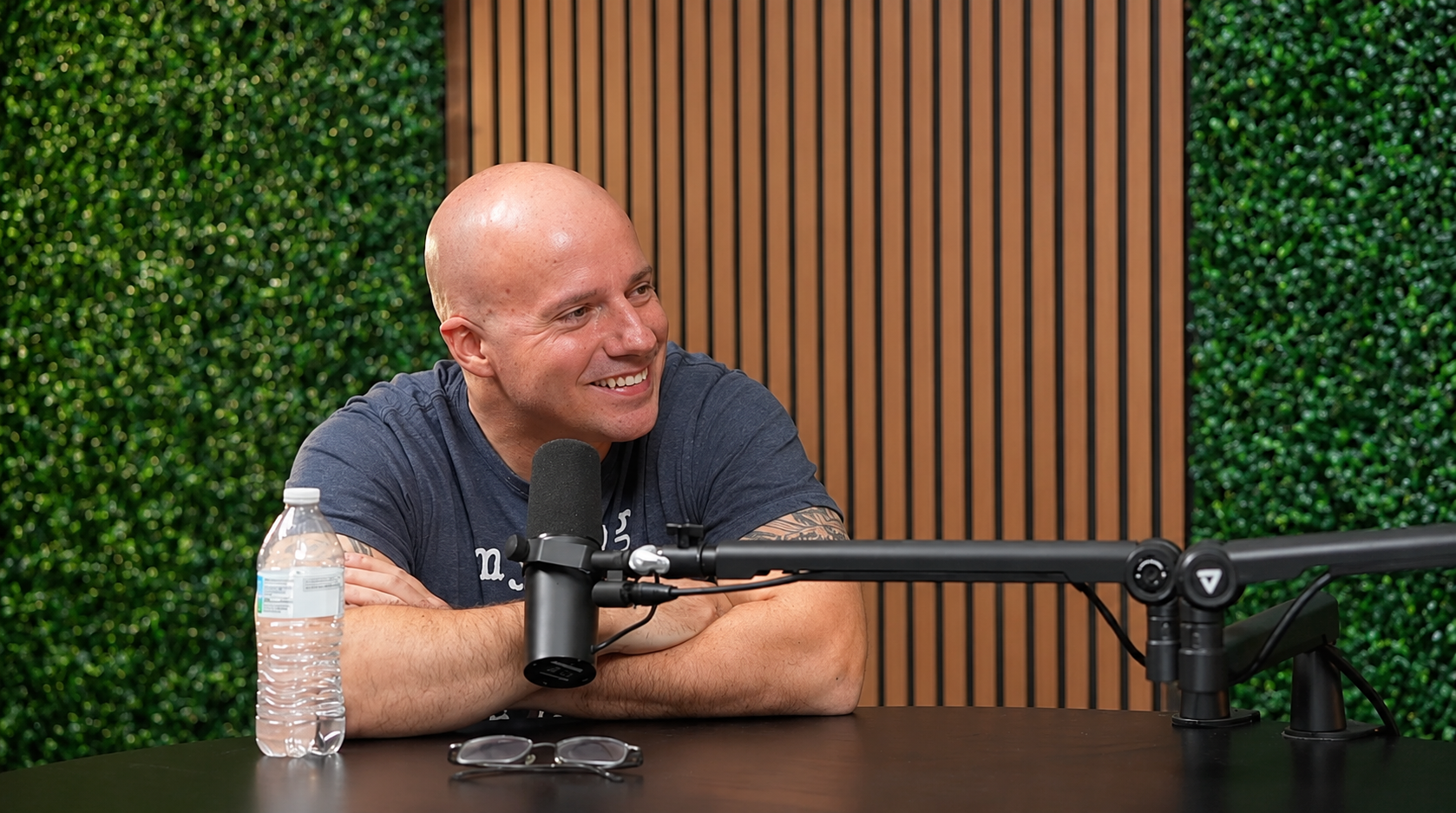 Calvin Smith smiling behind a podcast microphone in a studio with a green plant wall